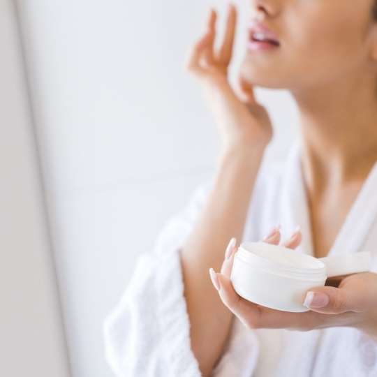 Person applying face cream in robe.