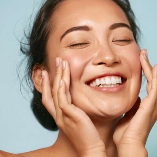 Smiling person with hands on face, eyes closed