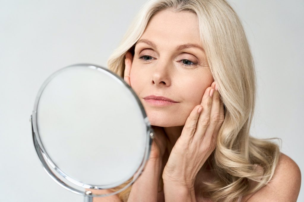 Closeup portrait middle age 50 woman looking at mirror, touching healthy skin.