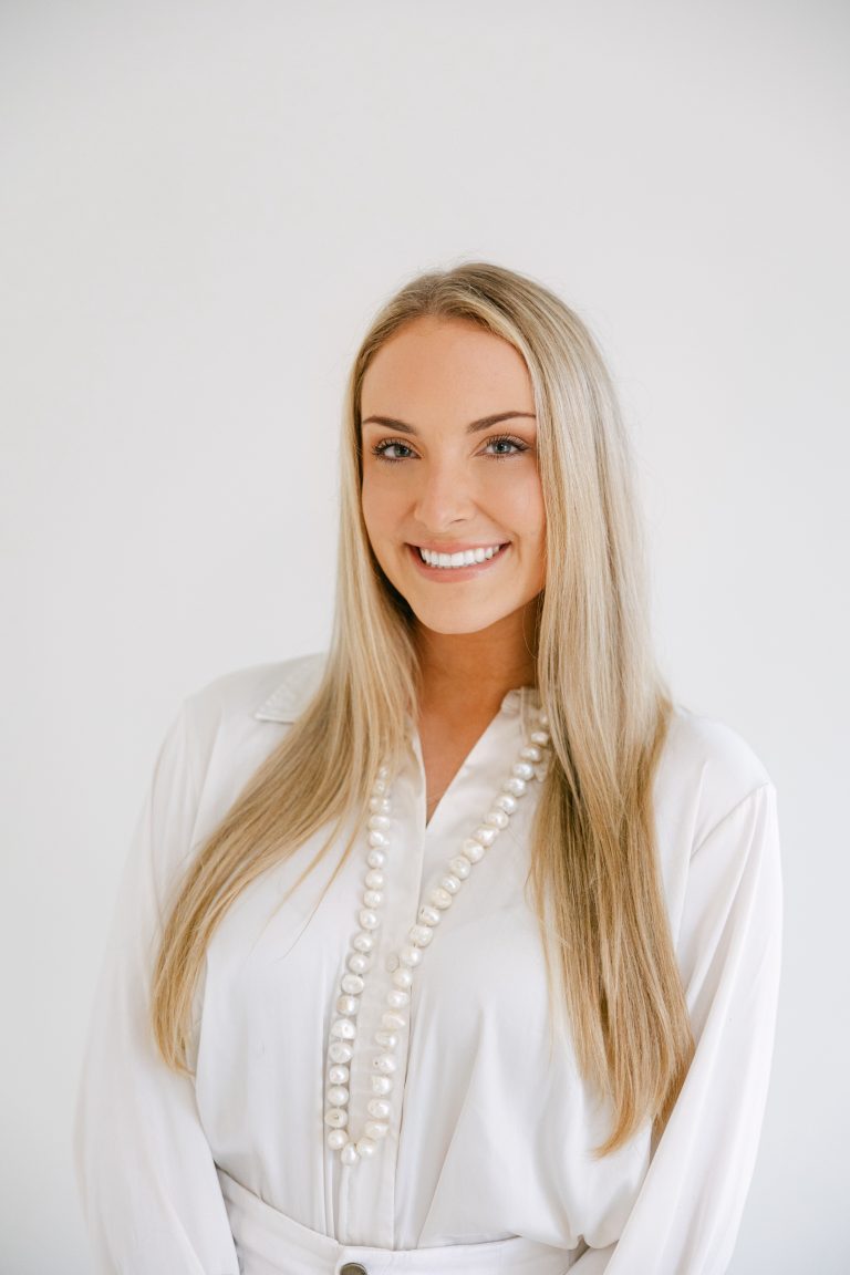 Woman smiling in white blouse with pearls.