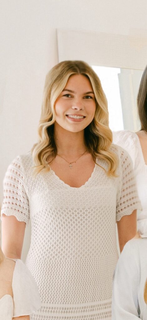 Woman in white crochet dress smiling indoors.