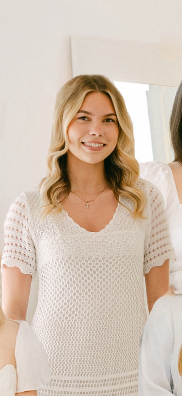 Woman in white crochet dress smiling indoors.